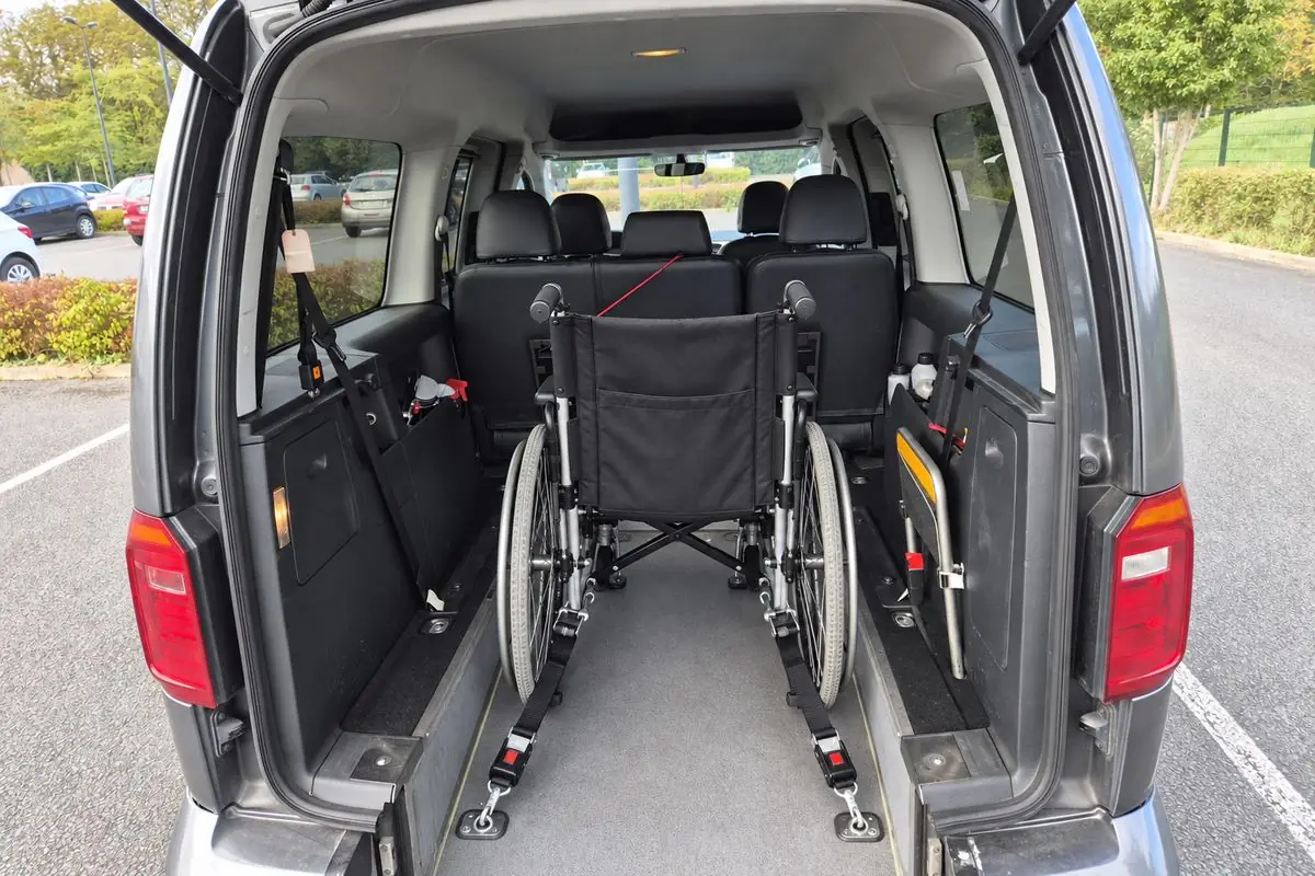 Un fauteuil roulant arrimé par des sangles au plancher du taxi JB TRANSPORT, vu depuis le hayon ouvert
