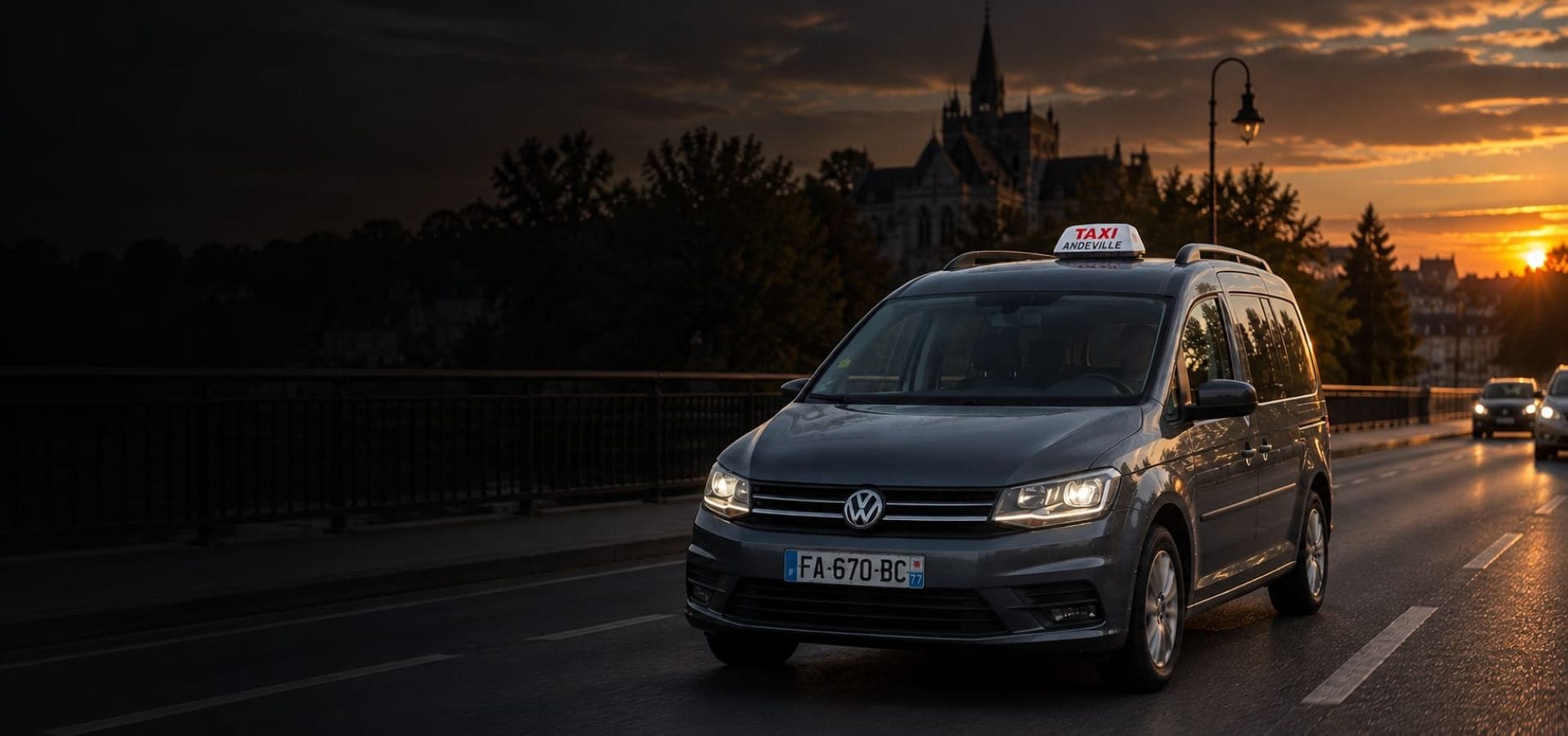 Le taxi JB TRANSPORT, un Volkswagen Caddy Maxi gris, roulant phares allumés au coucher du soleil